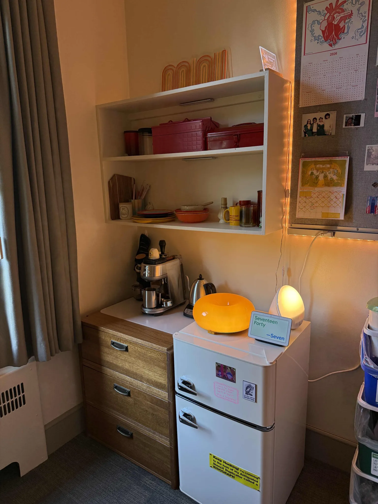 A mini fridge, espresso machine, and shelves in a dorm corner.