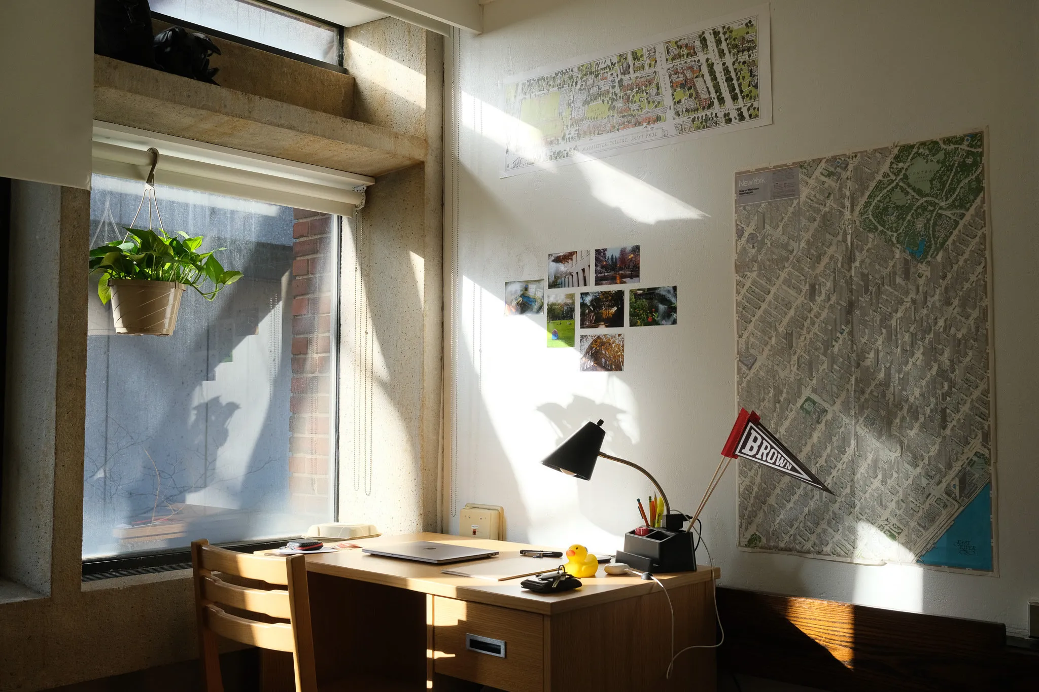 A sunlit dorm desk below a window, with maps on the wall.